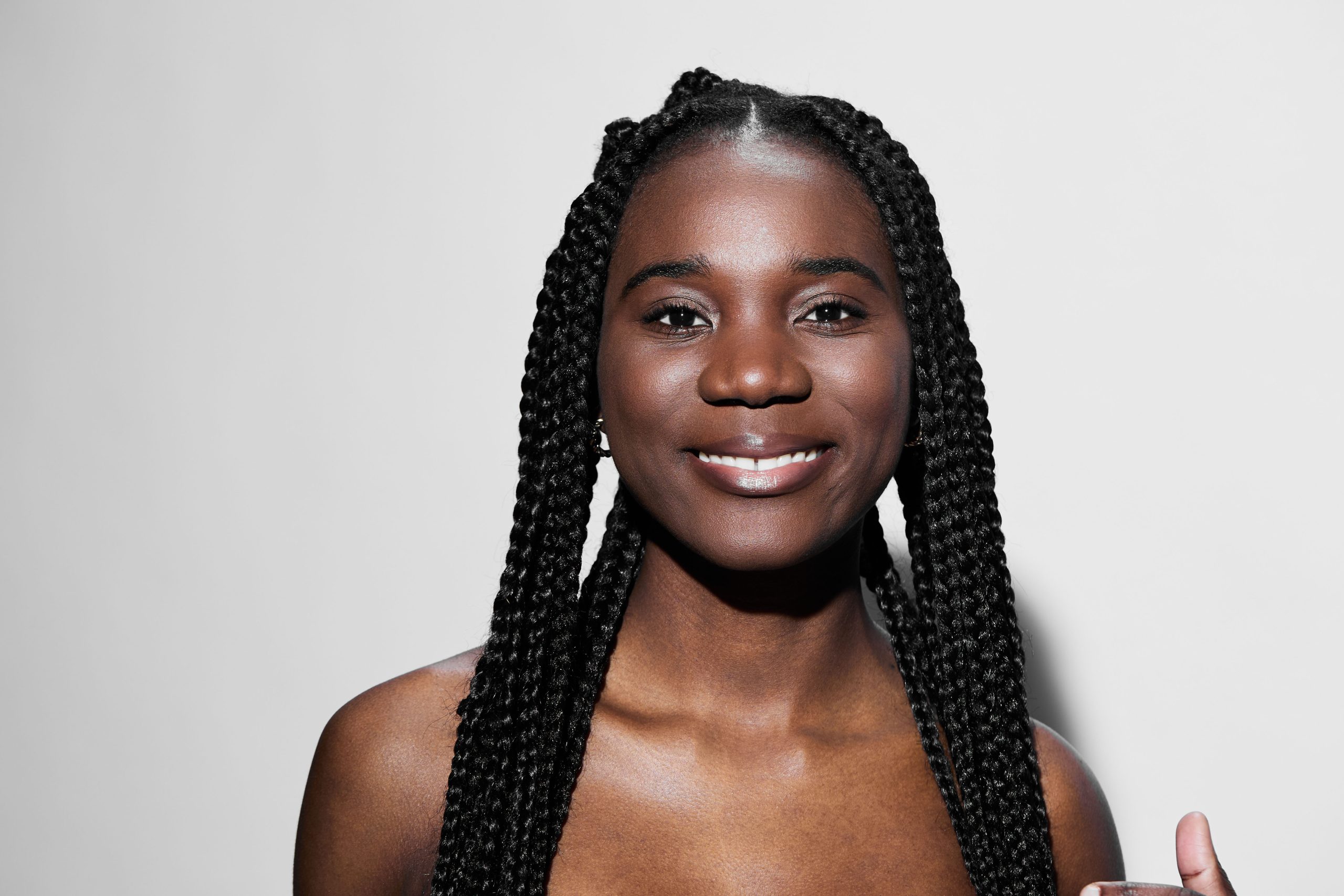 Smiling young woman with braided hair, showcasing healthy skin and vibrant smile against a neutral background, perfect for beauty and wellness themes
