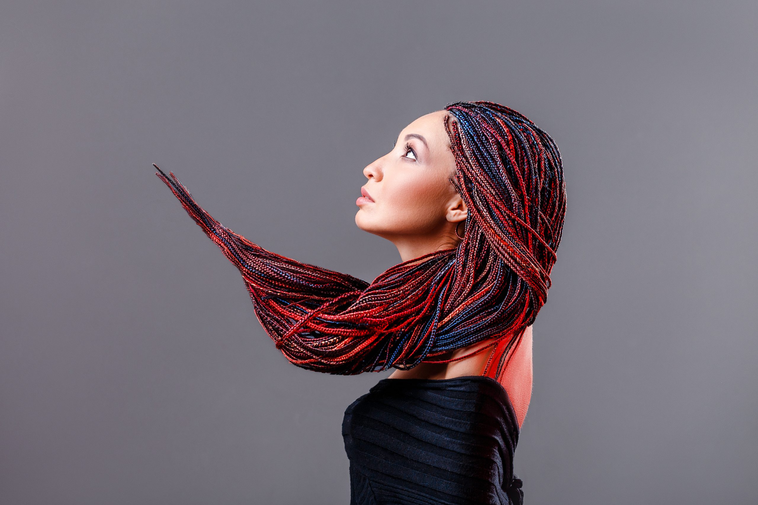 Fashion studio shoot of a mixed race woman with a creative colorful hairstyle in the form of a pigtail braided from dreadlocks in the technique of zizi. The concept of hairdressing art